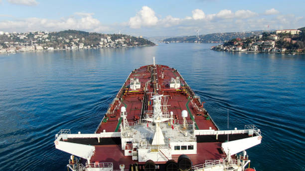 High-angle view from the deck of a red cargo ship traveling through a narrow waterway.