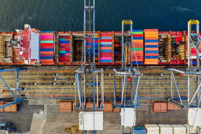 Aerial top-down view of a container ship docked at a port terminal with cranes.